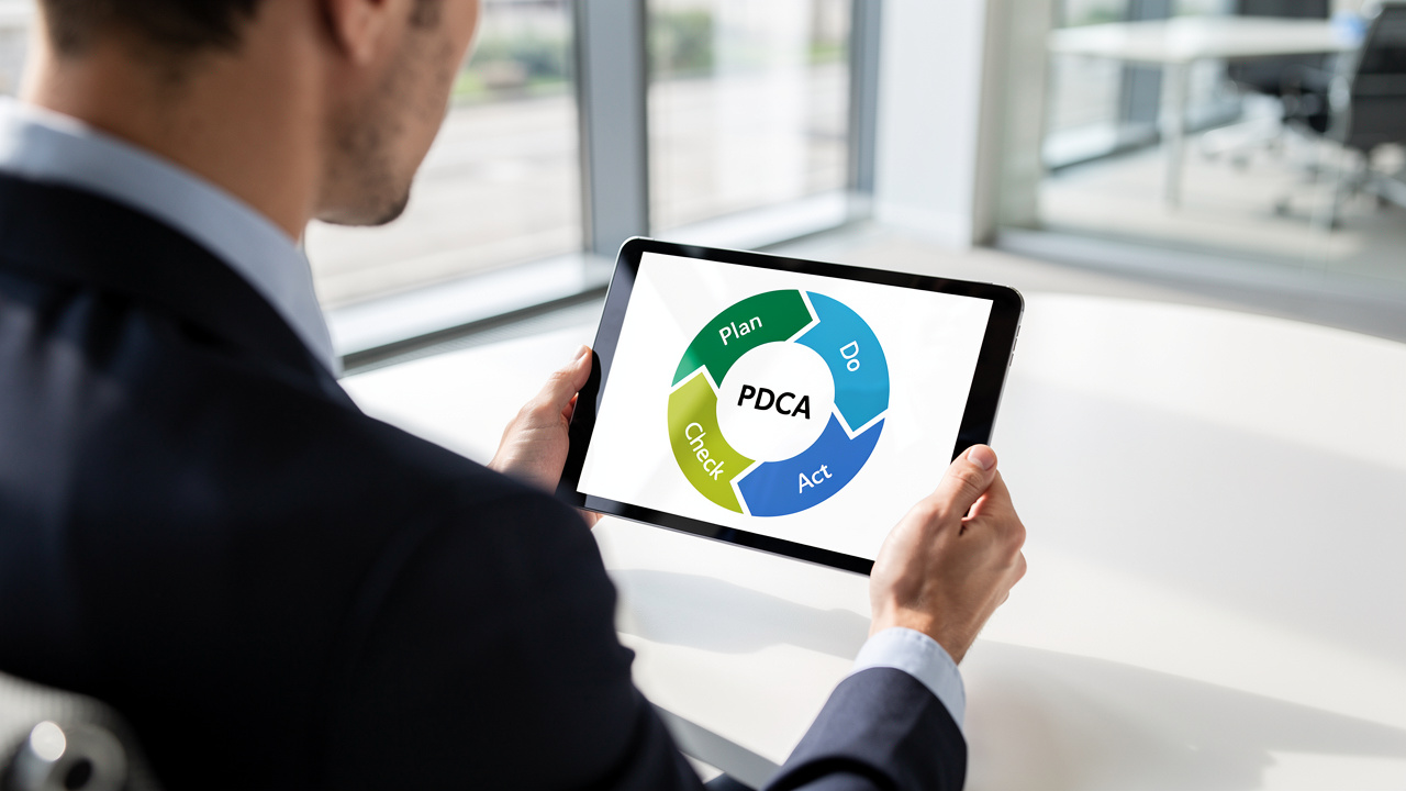 Profissional analisando diagrama do ciclo PDCA em tablet em ambiente corporativo iluminado