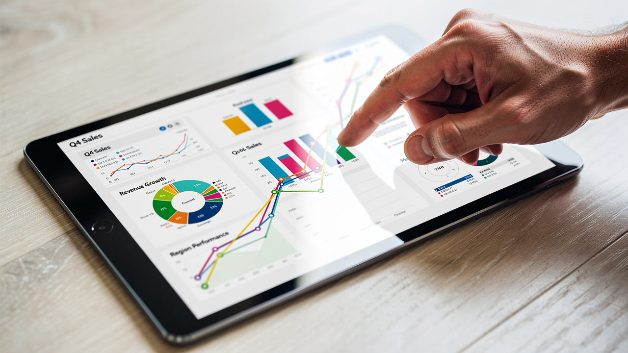 Tela de tablet exibindo gráficos coloridos de análise de vendas com uma mão apontando para um dado específico